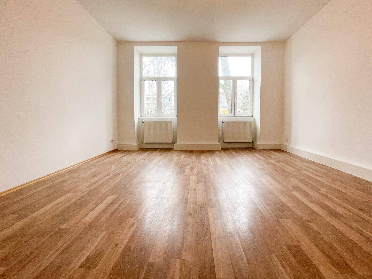 Geräumiger, heller Raum mit Parkettboden und zwei großen Fenstern, bereit zum Einzug.