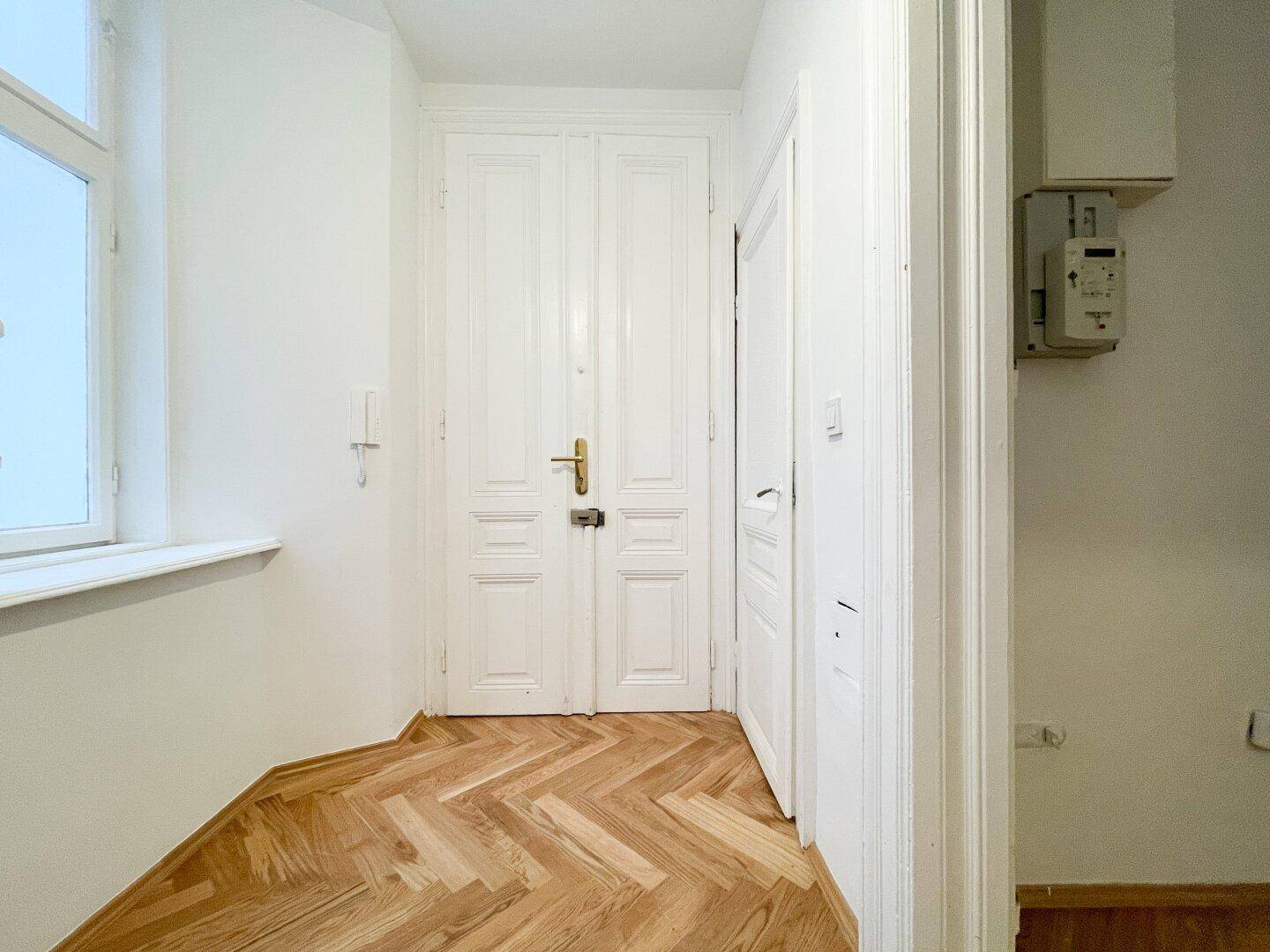 Eingangsbereich mit klassischem Fischgrätparkett, Doppeltür und einem Fenster für natürliches Licht.