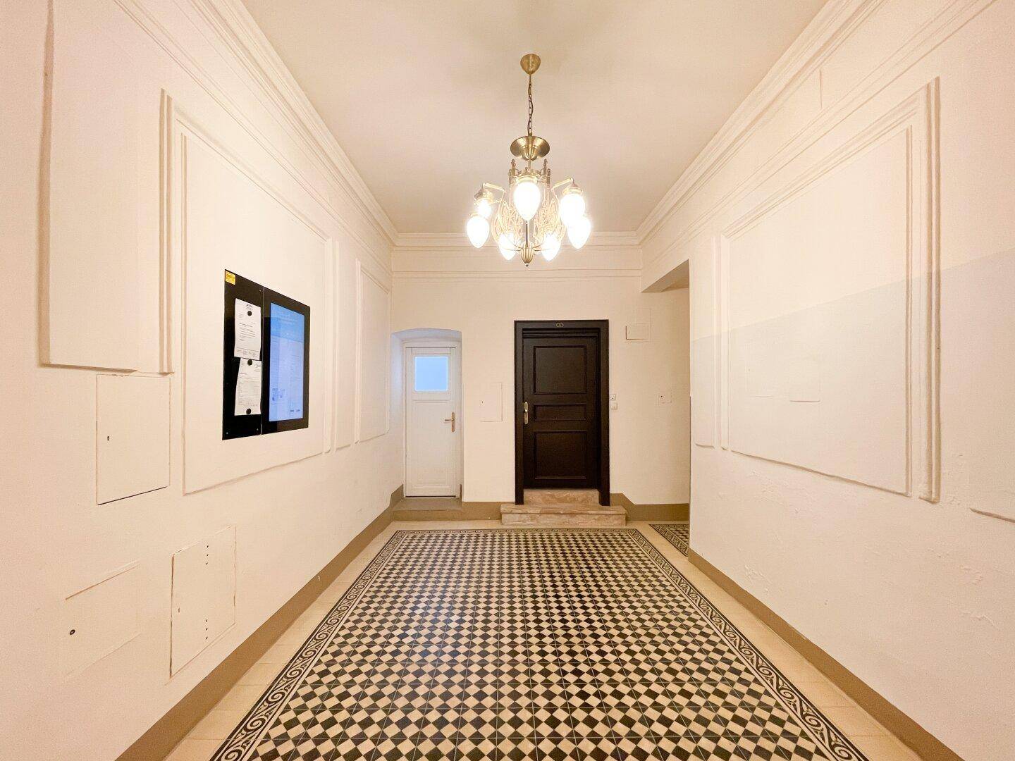 Repräsentativer Eingangsbereich mit Schachbrettmuster-Fliesenboden, hohen Decken und elegantem Kronleuchter.