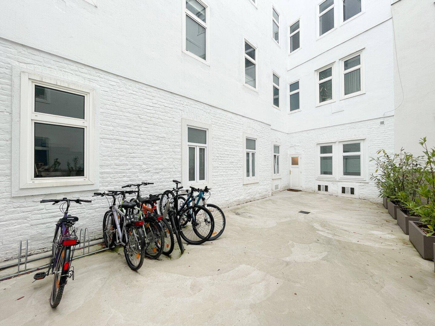 Heller Innenhof mit Fahrradabstellplätzen und kleinen Pflanzen in Kübeln, die für Grün sorgen.