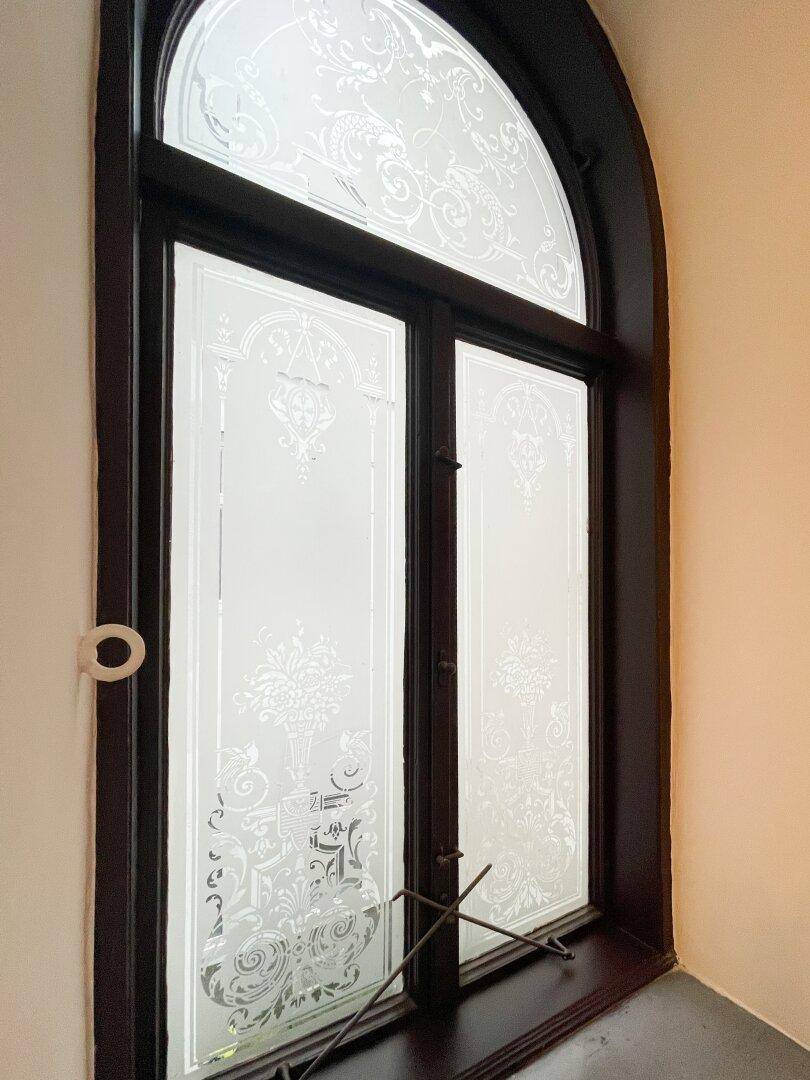 Detailaufnahme eines eleganten Fensters mit geätztem Glas und floralen Mustern, das den Altbaucharme unterstreicht.
