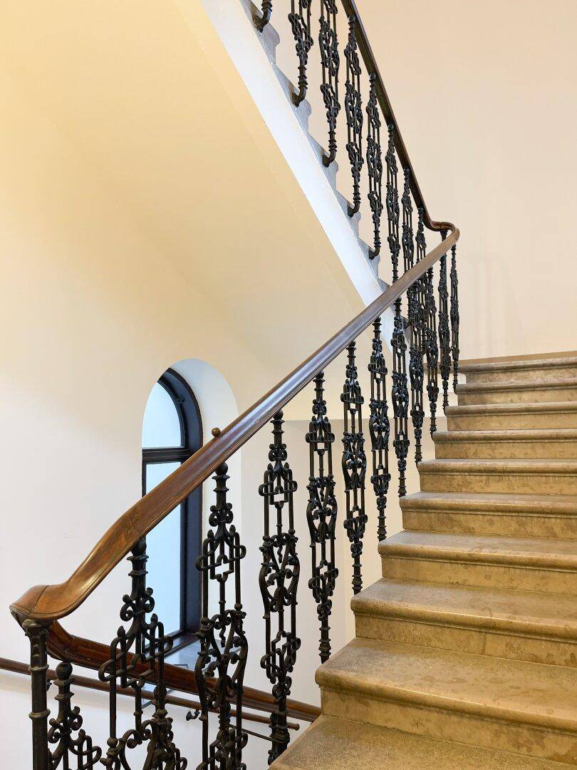 Historisches Treppenhaus mit Steinstufen, schmiedeeisernem Geländer und elegantem Holzhandlauf.