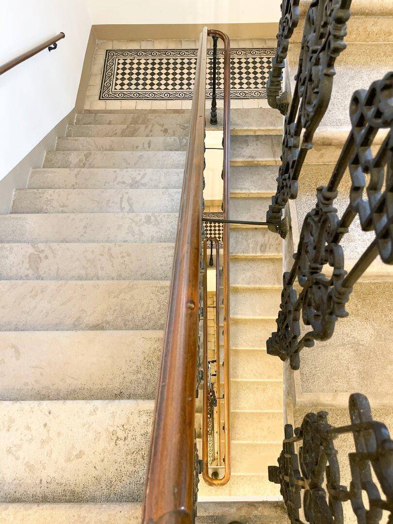 Blick von oben auf die Steintreppe mit schmiedeeisernem Geländer und elegantem Holzhandlauf.