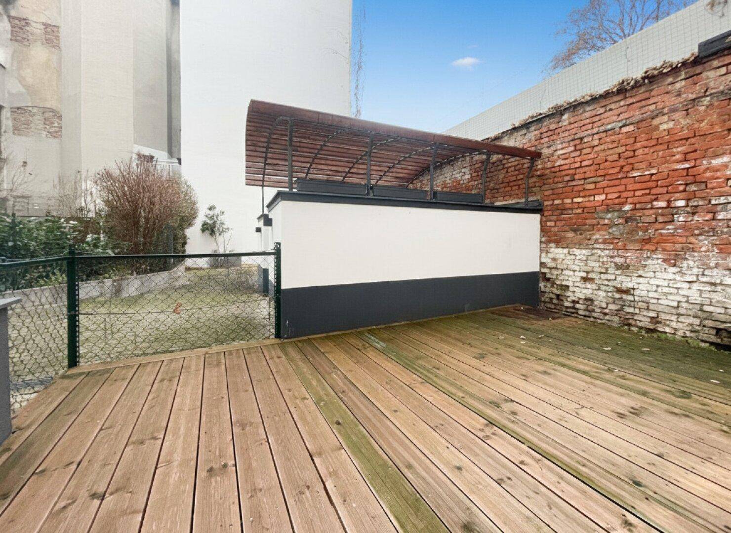 Eine weitläufige Holzterrasse grenzt an einen kleinen Gartenbereich mit einer Ziegelmauer im Hintergrund.