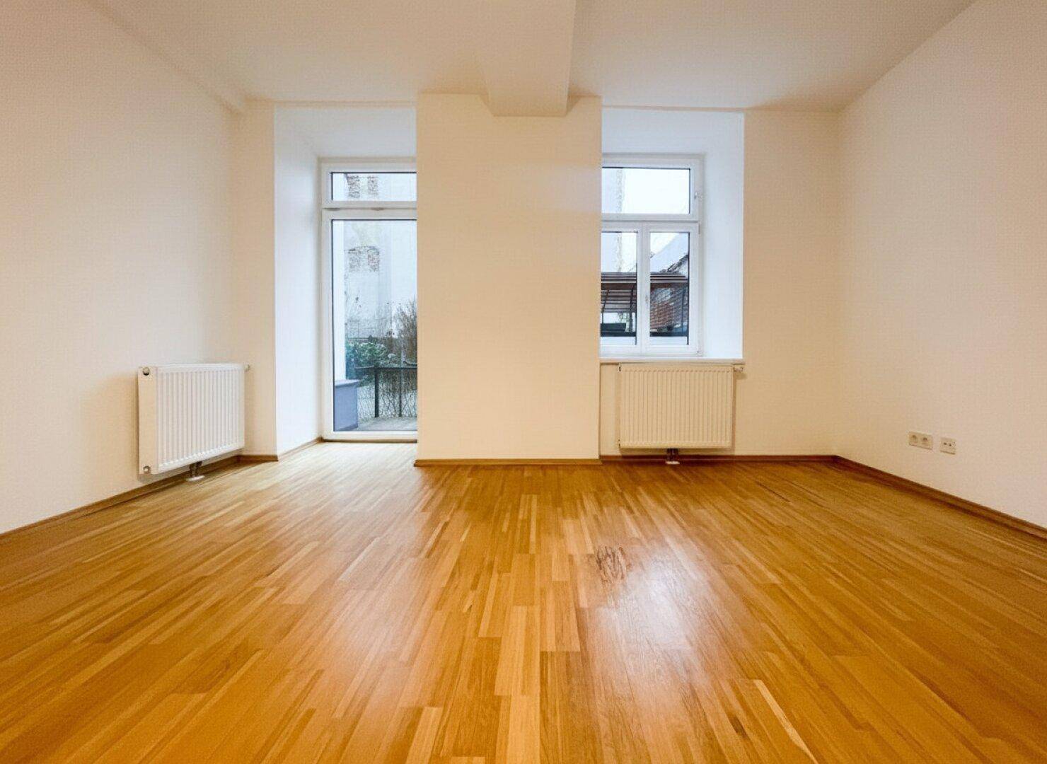 Helles, leeres Zimmer mit Parkettboden und großen Fenstern, bereit für individuelle Gestaltung.