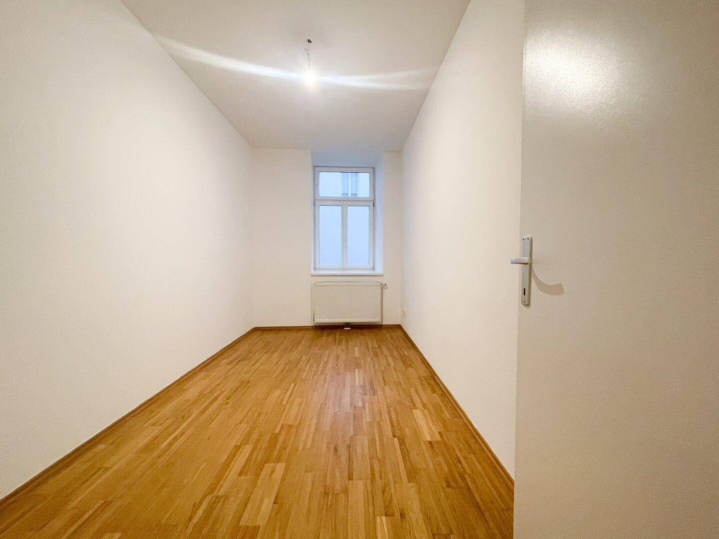 Schmaler, heller Raum mit Parkettboden und einem Fenster, ideal als Schlaf- oder Arbeitszimmer.