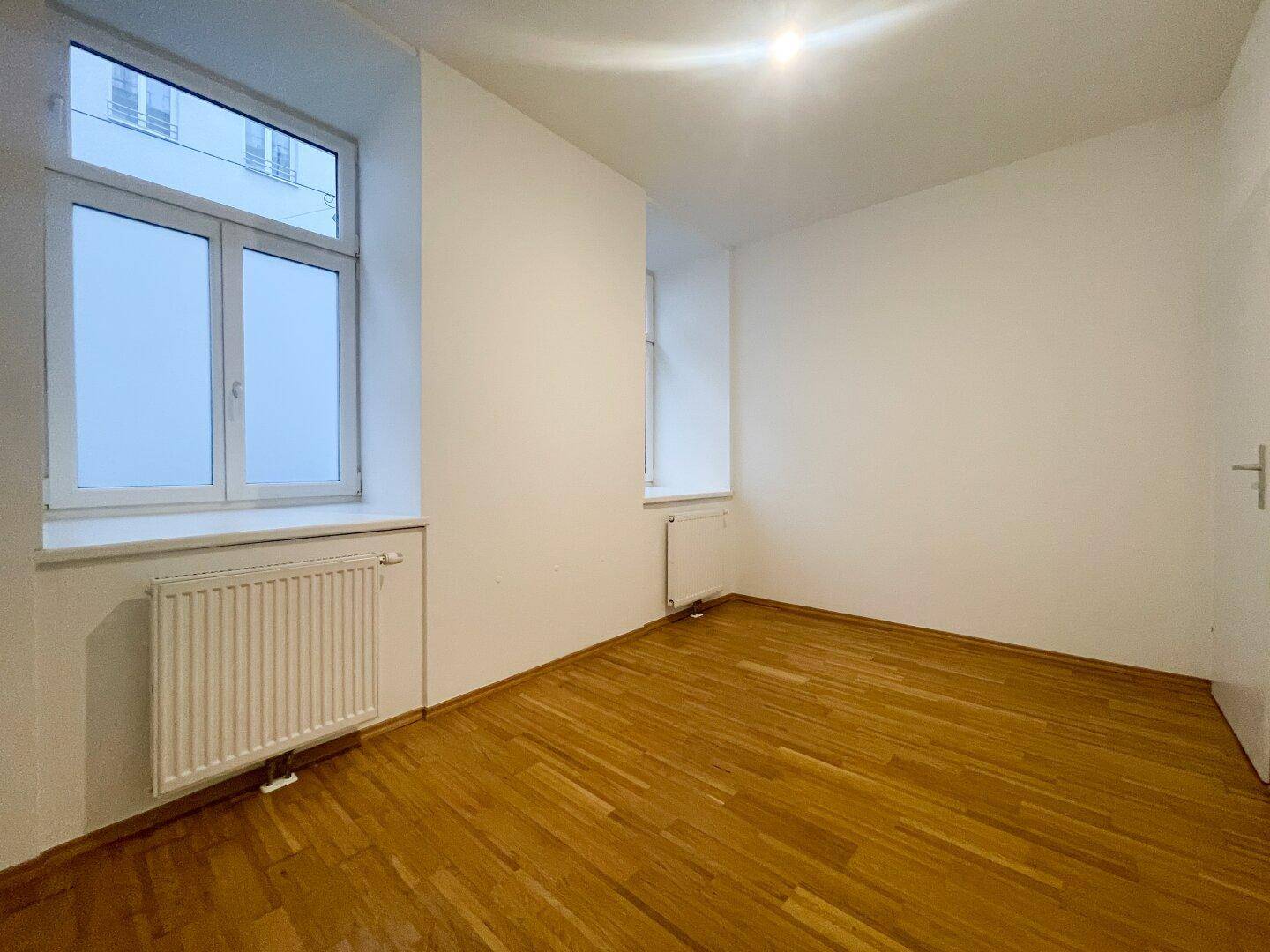 Helles Zimmer mit zwei Fenstern und Parkettboden, bietet viel natürliches Licht.