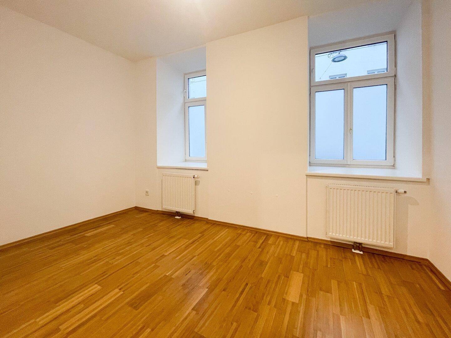 Geräumiges, helles Zimmer mit Parkettboden und zwei Fenstern, ideal als Schlafzimmer.