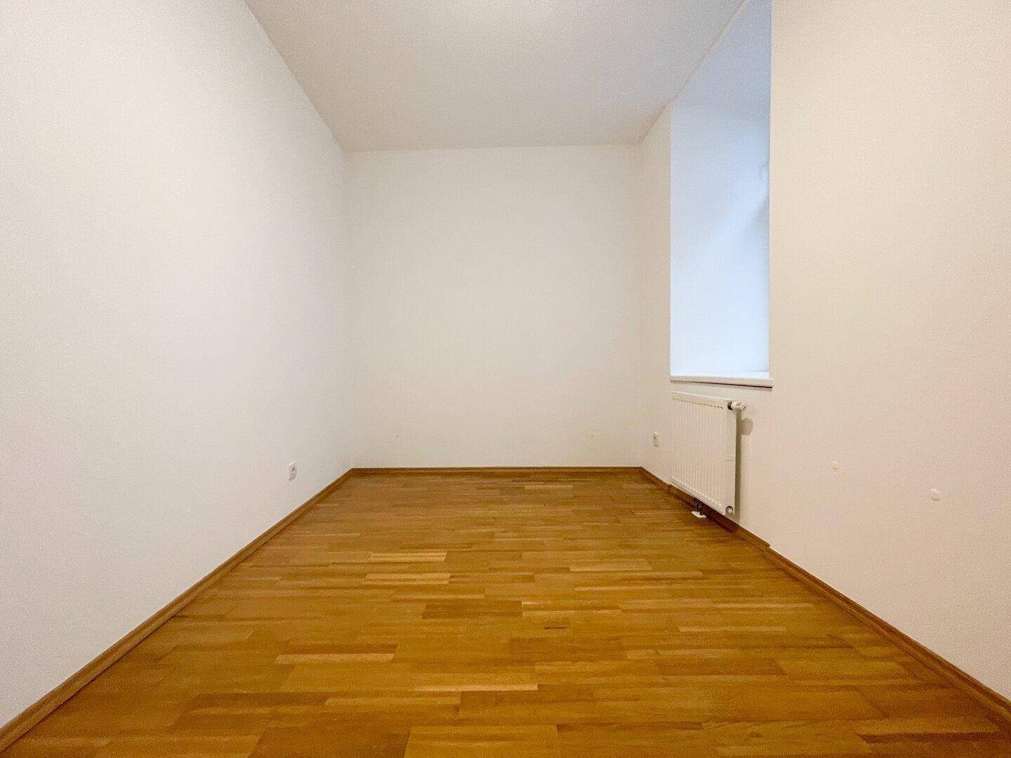 Langer, heller Raum mit Parkettboden und einem Fenster, vielseitig nutzbar.