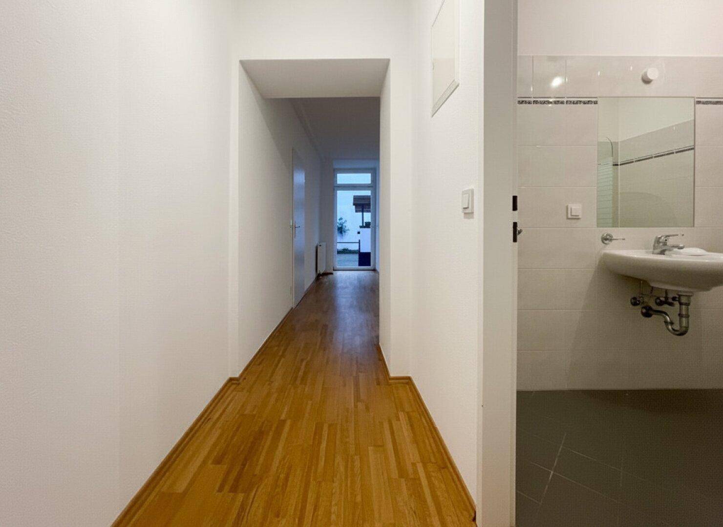 Heller Flur mit Parkettboden, der zu weiteren Räumen führt, mit Blick auf ein Badezimmer.