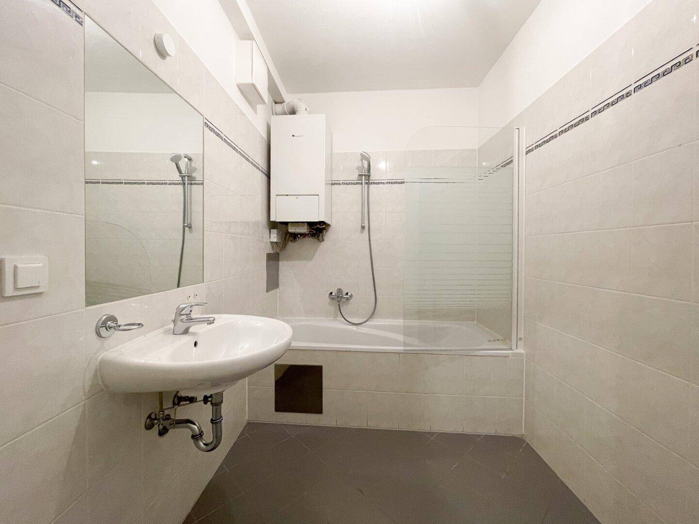 Funktionales Badezimmer mit Badewanne, Duschabtrennung, Waschbecken und hellen Fliesen.