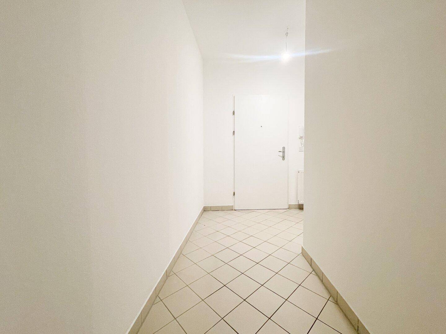 Langer, heller Flur mit diagonal verlegten Fliesen, führt zum Eingangsbereich.