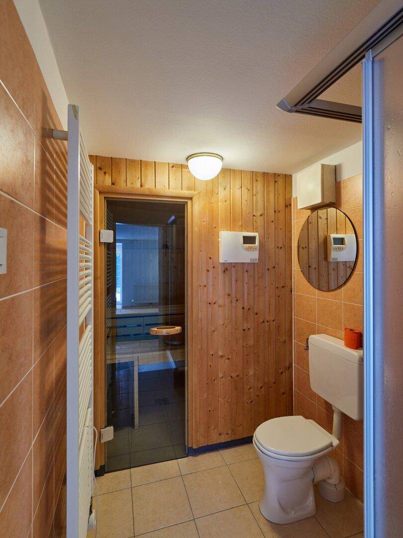 Funktionales Badezimmer mit Terrakotta-Fliesen, WC, beheiztem Handtuchhalter und Saunazugang.