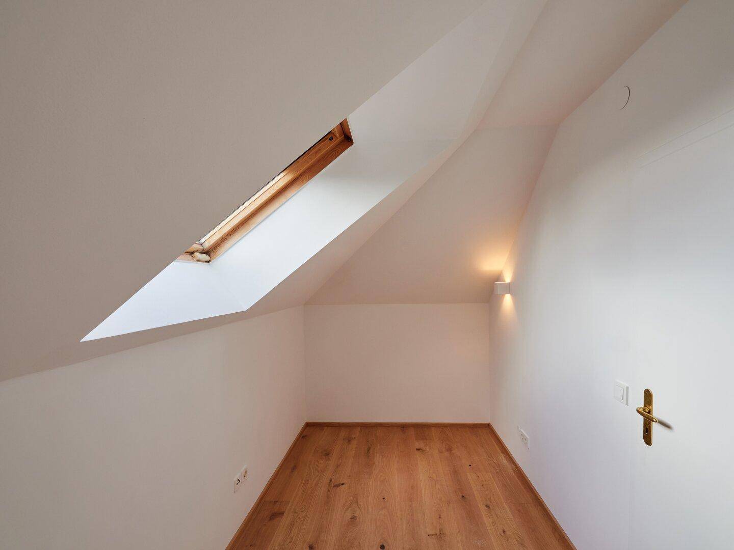 Kleiner Abstellraum mit Holzboden, Dachschräge und einem Dachfenster für natürliches Licht.