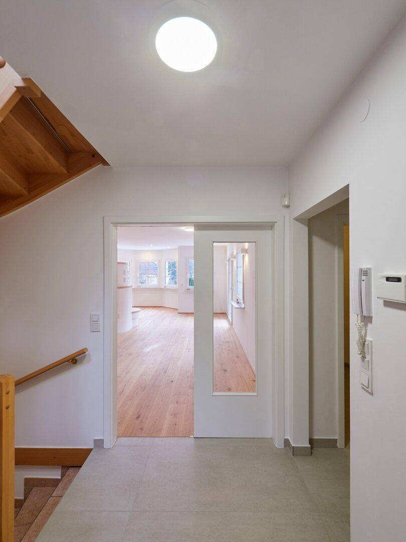 Heller Flur mit Fliesenboden und Holzwangentreppe, der zum offenen Wohnbereich führt.