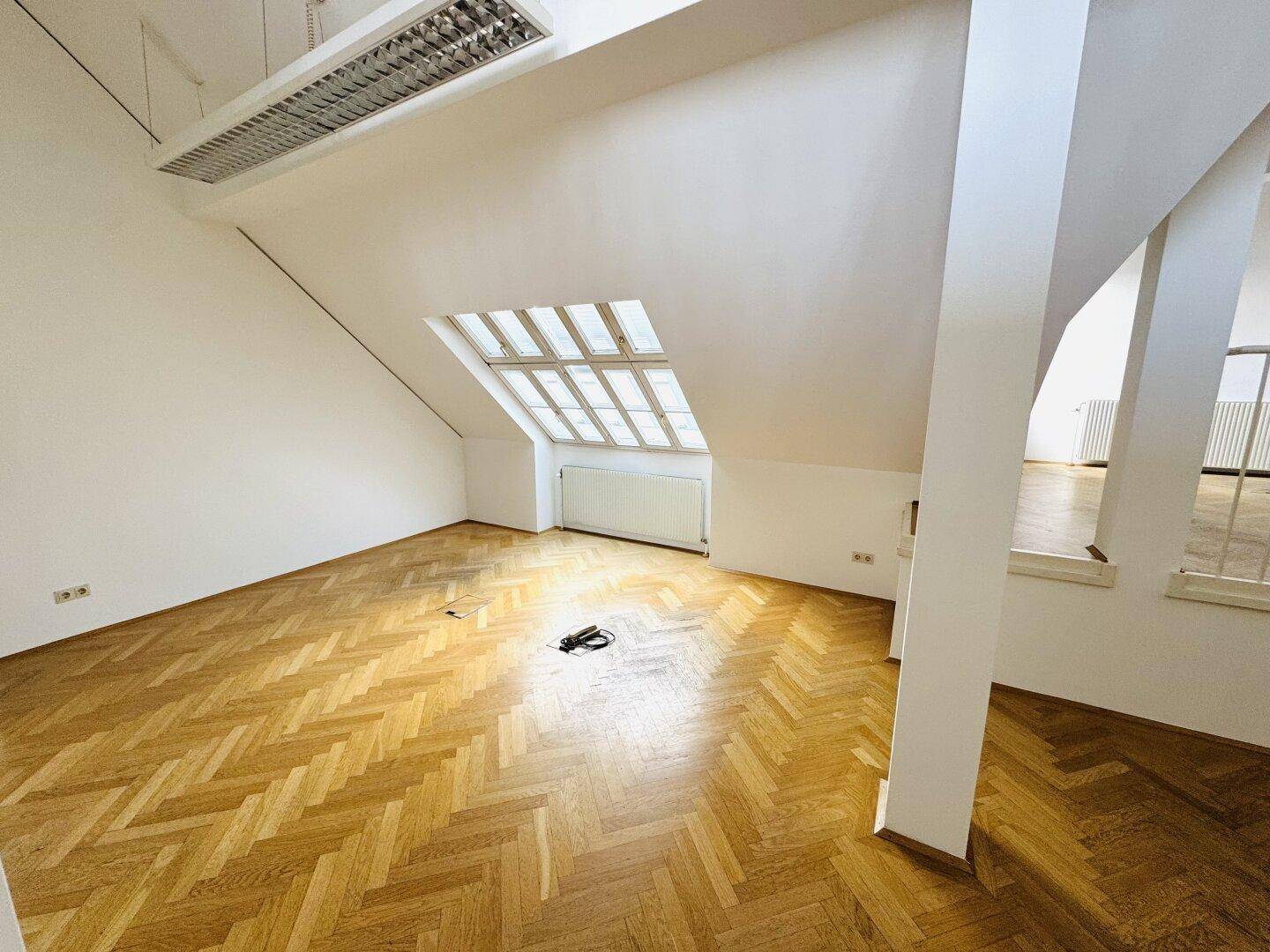 Geräumiger Dachgeschossraum mit Holzparkett, Dachfenster und schrägen Wänden.