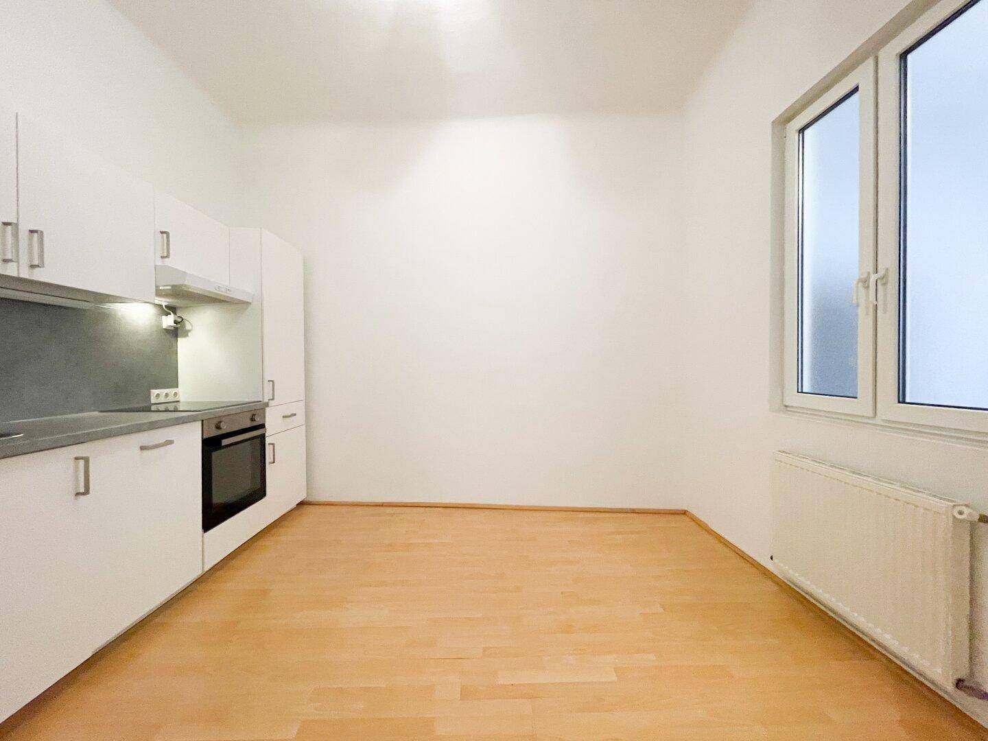 Kleine, funktionale Küche mit hellen Schränken, Herd und Fenster für Tageslicht.