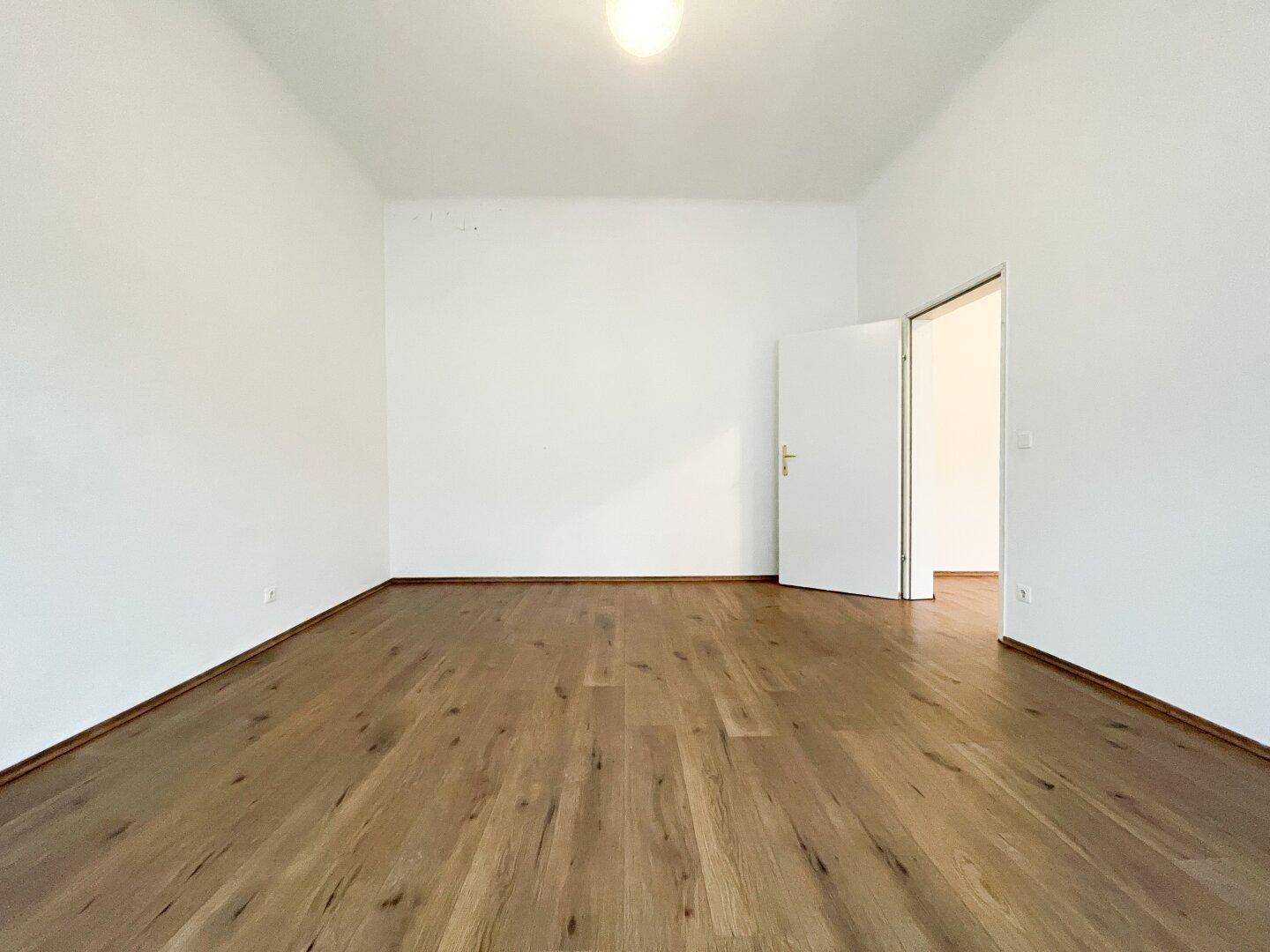 Geräumiger, heller Raum mit Holzboden und offener Tür, ideal für ein Schlafzimmer.