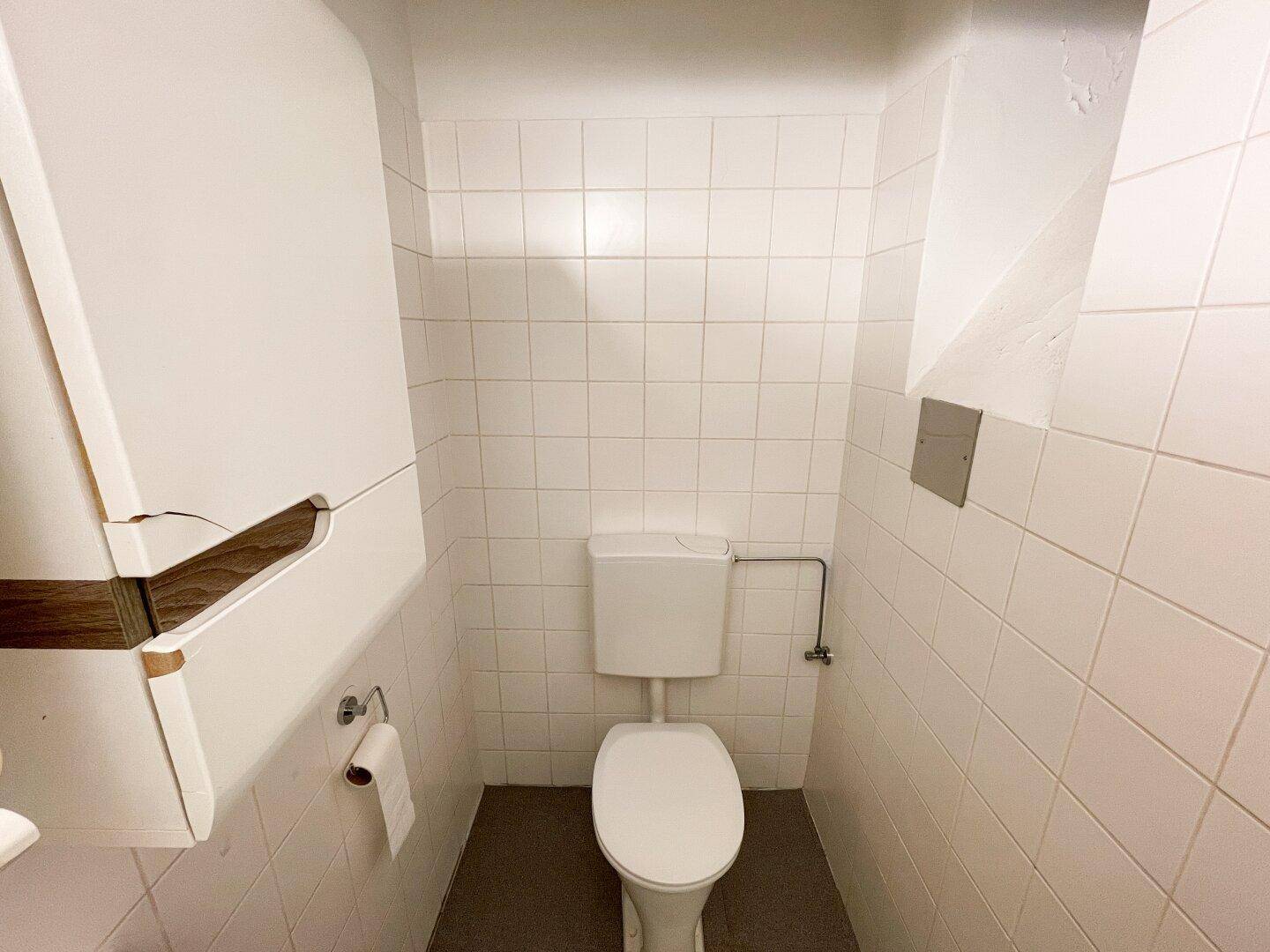 Separate Toilette mit weißen Fliesen und einfacher Ausstattung.