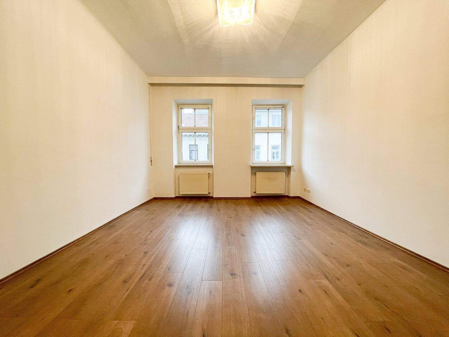 Heller, leerer Raum mit neuem Holzboden und zwei Fenstern, bereit zur individuellen Gestaltung.