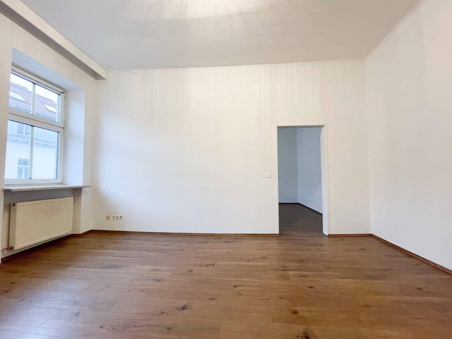 Lichtdurchfluteter Raum mit Holzboden und einem großen Fenster, ideal für Wohnzwecke.