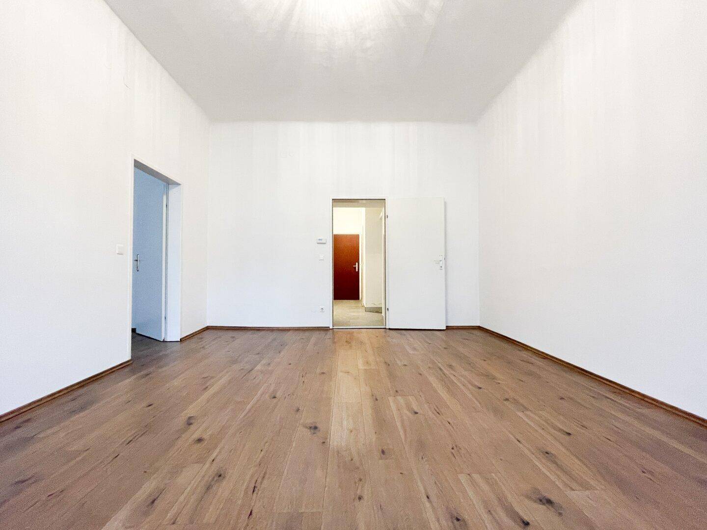 Großer, heller Raum mit Holzboden und mehreren Türen, bietet flexible Nutzungsmöglichkeiten.