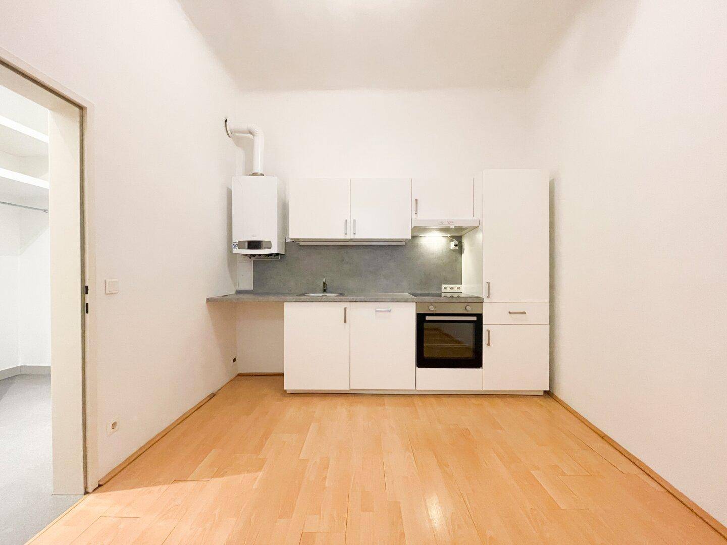 Kompakte Einbauküche mit weißen Schränken, Kochfeld und Warmwasserboiler.