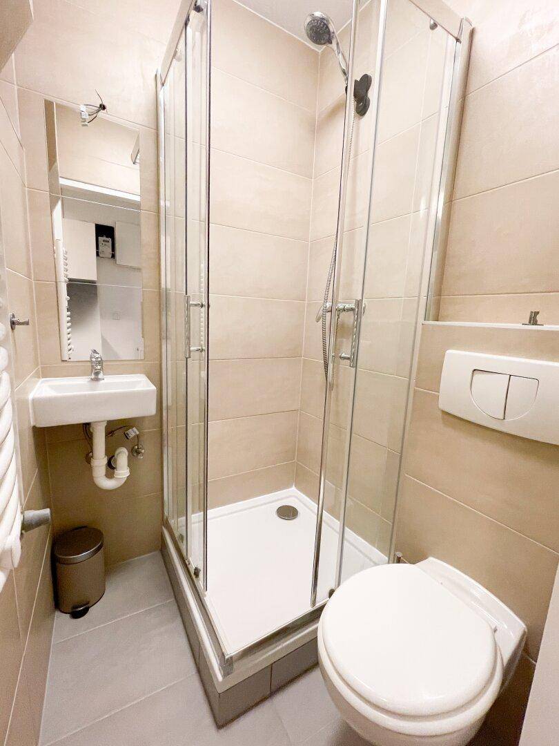 Kleines Badezimmer mit Duschkabine, WC, Waschbecken und beigefarbenen Fliesen, funktional und sauber.