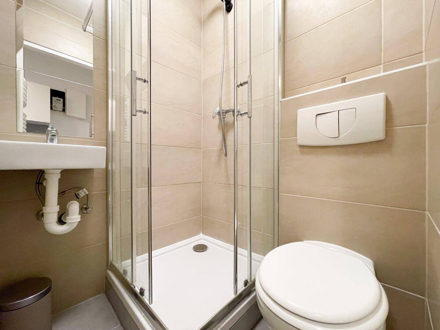 Detailansicht des Badezimmers mit Duschkabine, Toilette und beigefarbenen Wandfliesen, gut gepflegt.