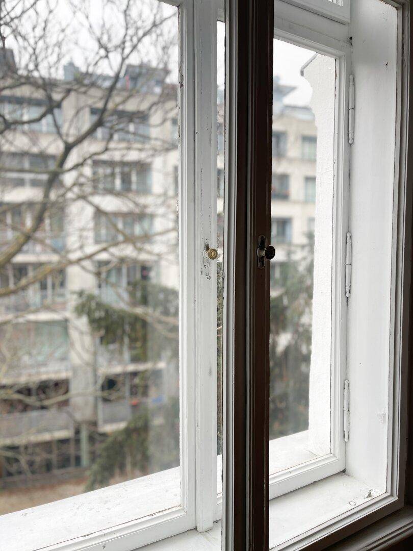Blick aus einem geöffneten Fenster auf die umliegenden Gebäude und Bäume, typisch für die Stadt.