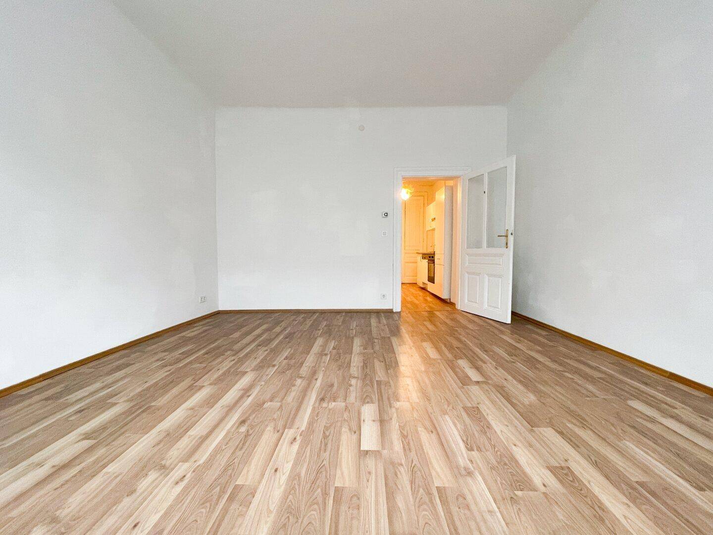 Geräumiger, heller Raum mit Laminatboden und Zugang zu einem weiteren Zimmer, ideal für Wohnzwecke.