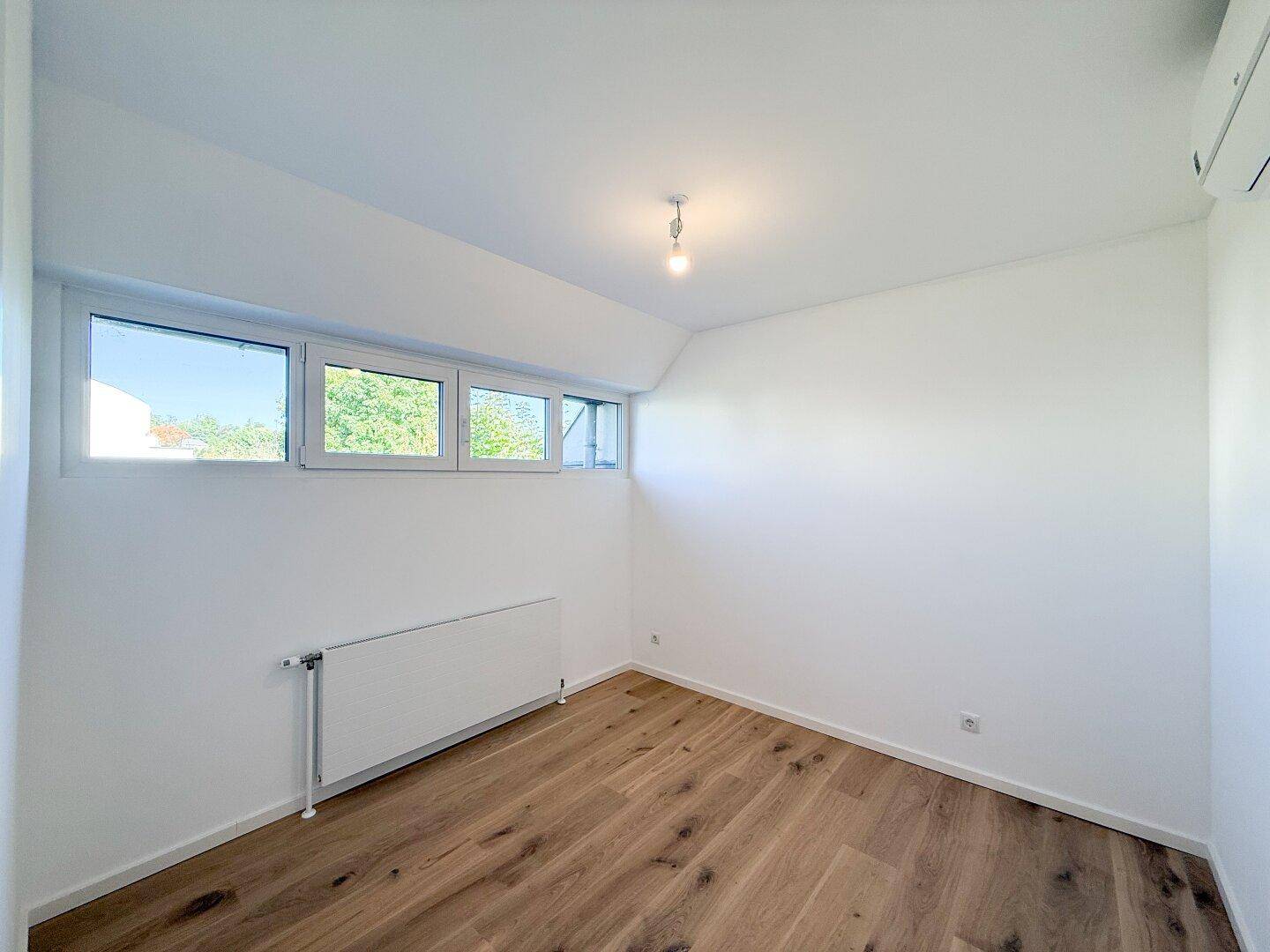 Helles Schlafzimmer mit Holzboden, weißen Wänden und breiten Fenstern für viel Tageslicht.