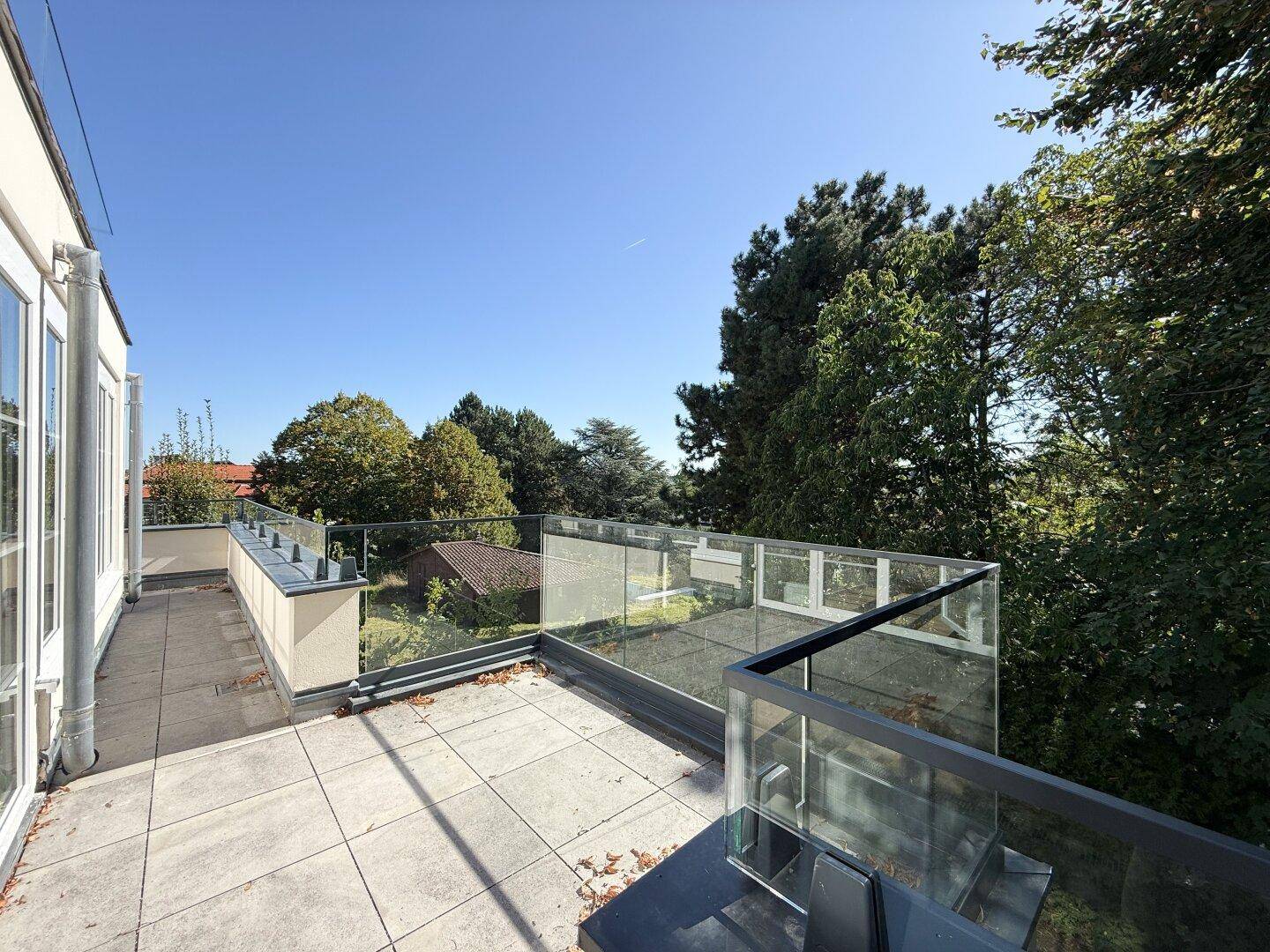 Große geflieste Terrasse mit modernem Glasgeländer und weitem Blick auf die Umgebung.