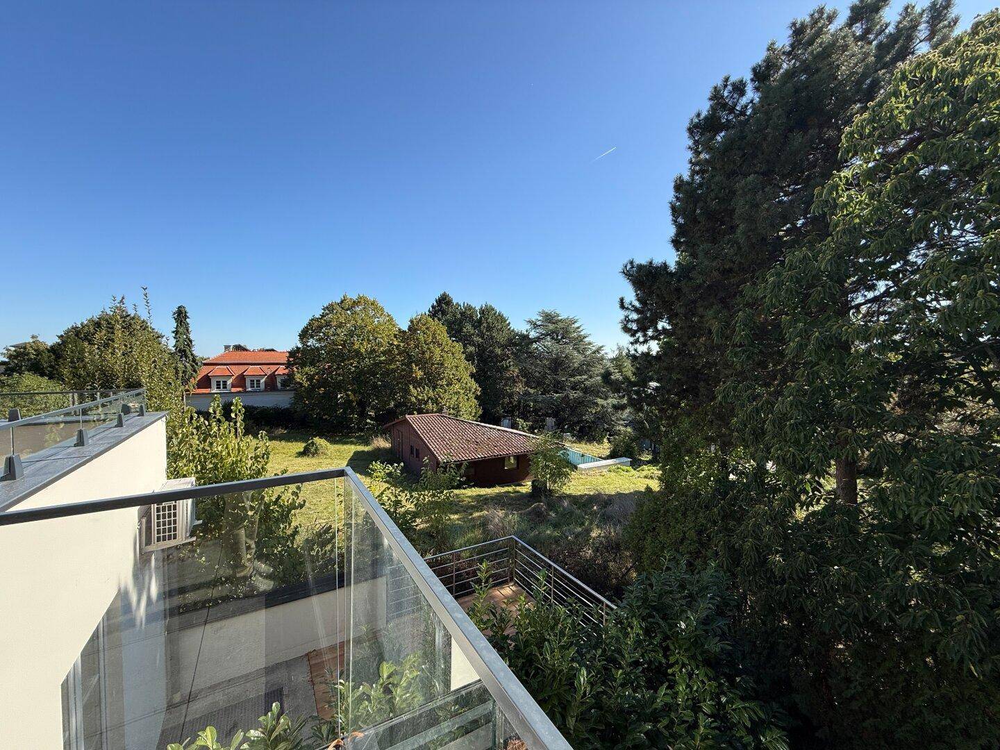 Weitläufiger Blick von der Terrasse auf einen grünen Garten und umliegende Häuser.