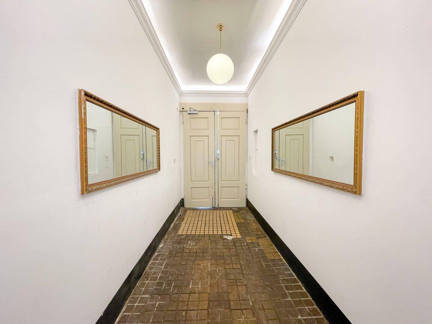 Langer, eleganter Hausflur mit zwei großen Spiegeln und traditionellem Bodenbelag, der zum Eingang führt.