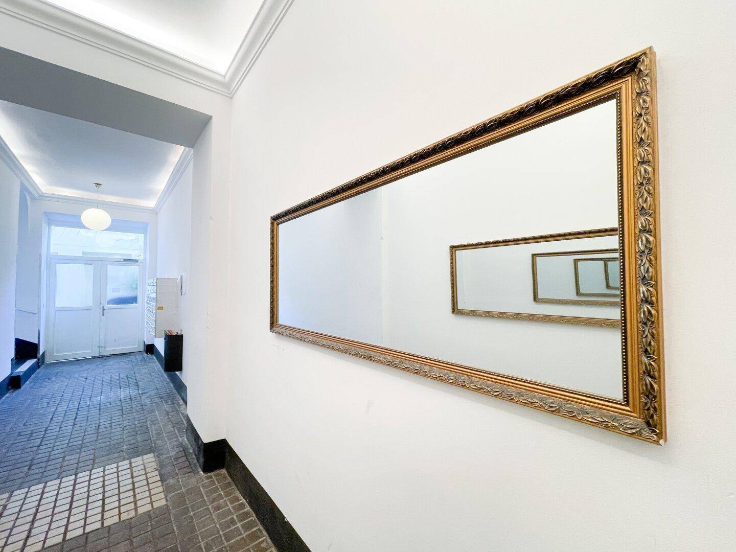Heller Hausflur mit großem Spiegel und traditionellem Fliesenboden, der den Altbaucharakter unterstreicht.