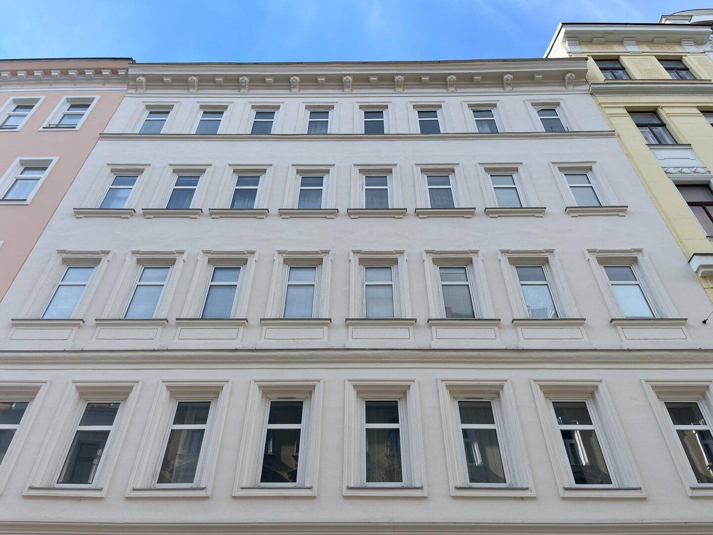 Die helle, frisch renovierte Fassade eines Mehrfamilienhauses mit vielen Fenstern unter blauem Himmel.