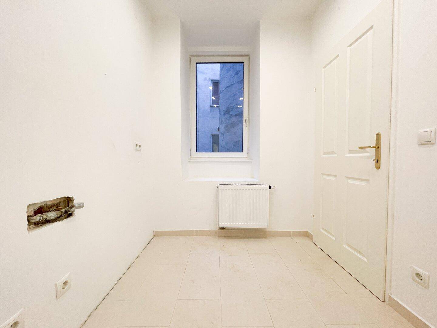 Heller Küchenraum mit Fenster, Heizkörper und Fliesenboden, ideal für eine moderne Küchengestaltung.