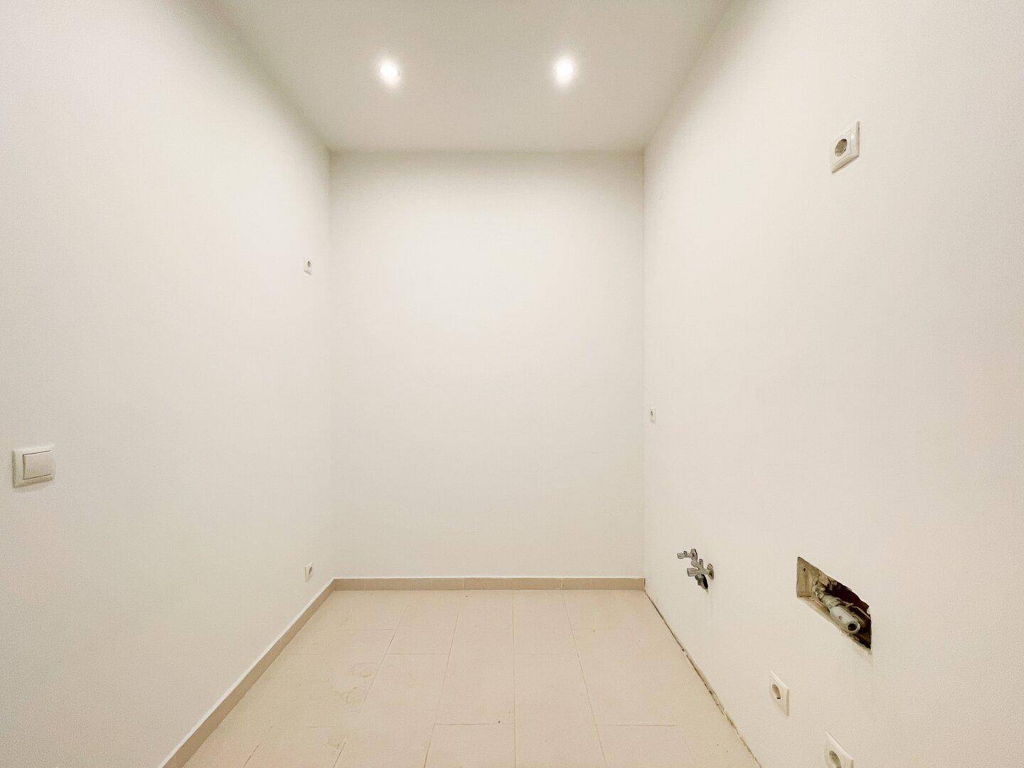 Unmöblierter Küchenbereich mit Fliesenboden und vorbereiteten Anschlüssen für die Installation einer Küche.