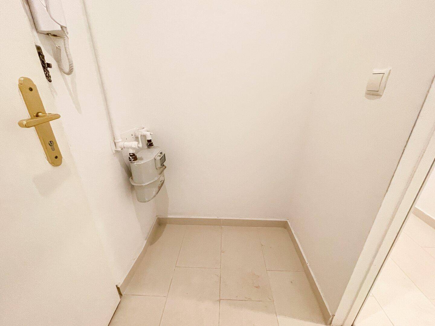 Kleiner Abstellraum oder Nische mit Gaszähler und Fliesenboden im Eingangsbereich des Apartments.