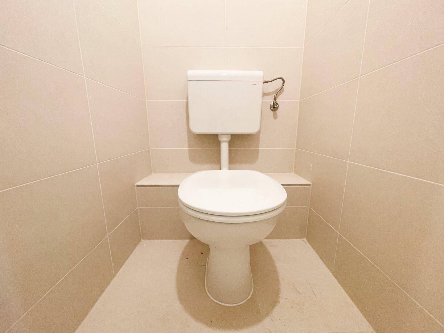 Separates WC mit beigefarbenen Fliesen an Wänden und Boden, in einem gepflegten Zustand.