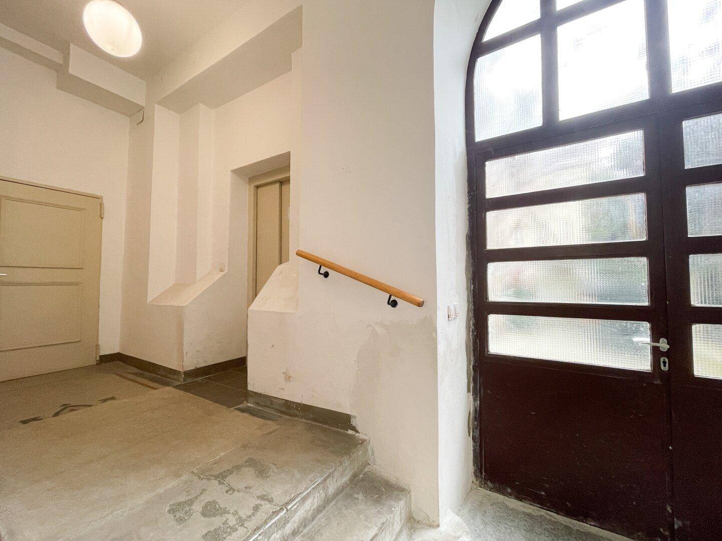 Eingangsbereich mit alter Holztür, Handlauf und Treppenaufgang in einem historischen Gebäude.