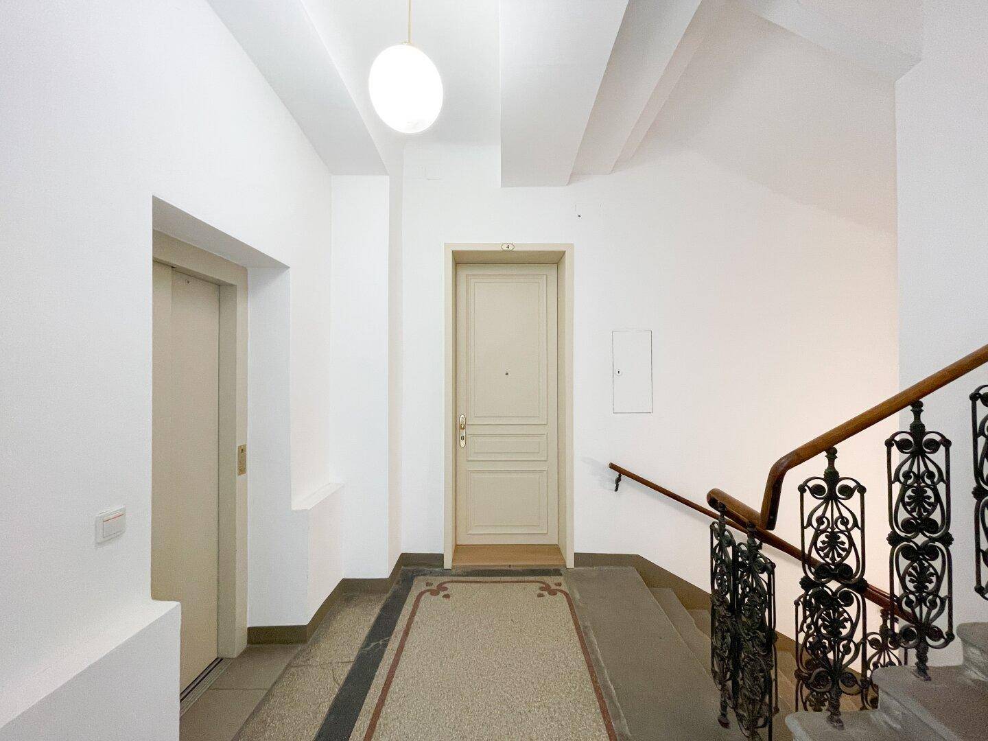 Heller Treppenabsatz mit Aufzug, Holztür und historischem Terrazzoboden in einem Altbau.