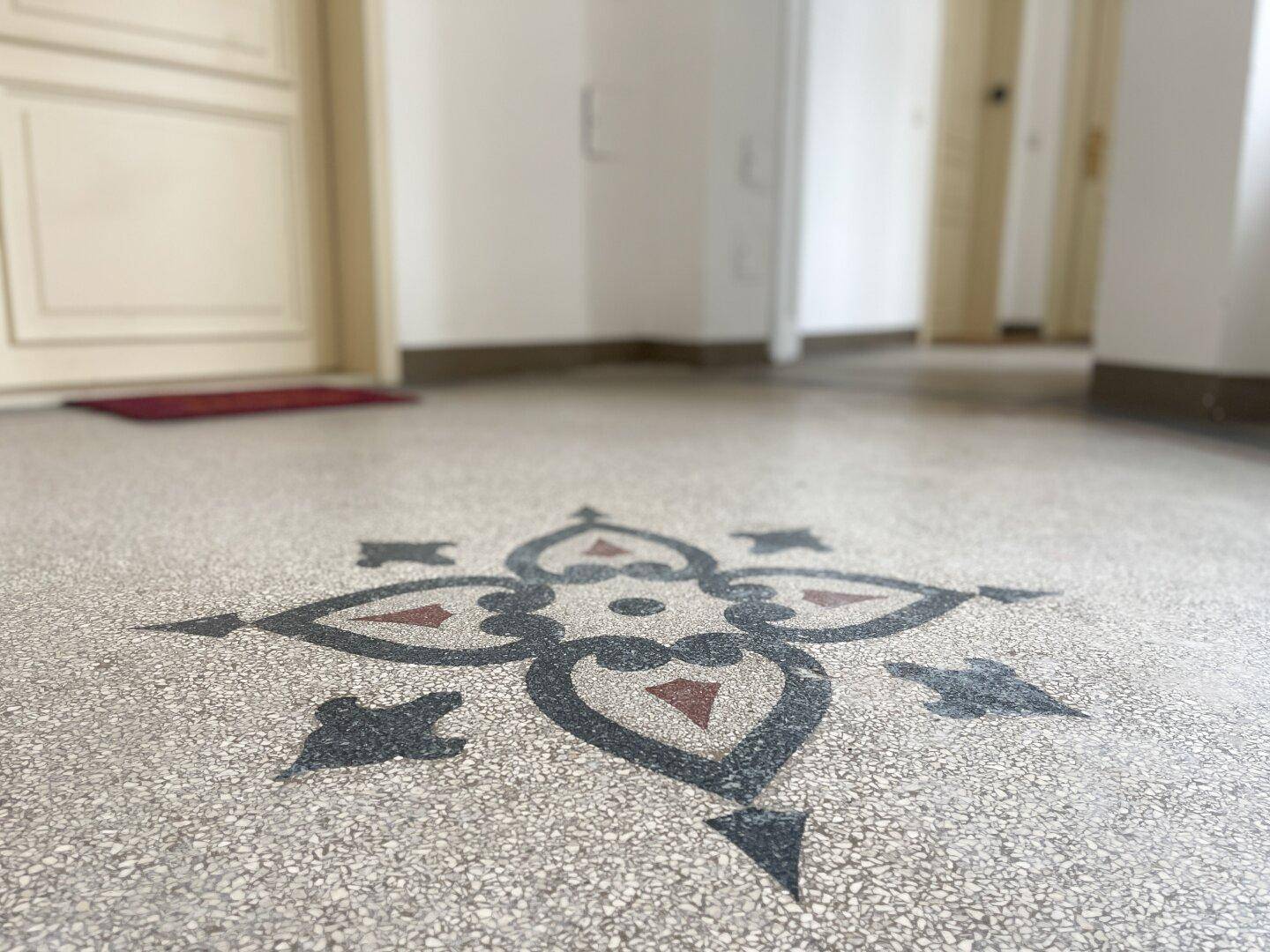 Detailaufnahme eines kunstvollen Terrazzobodens mit floralem Muster im Flur eines Altbaus.