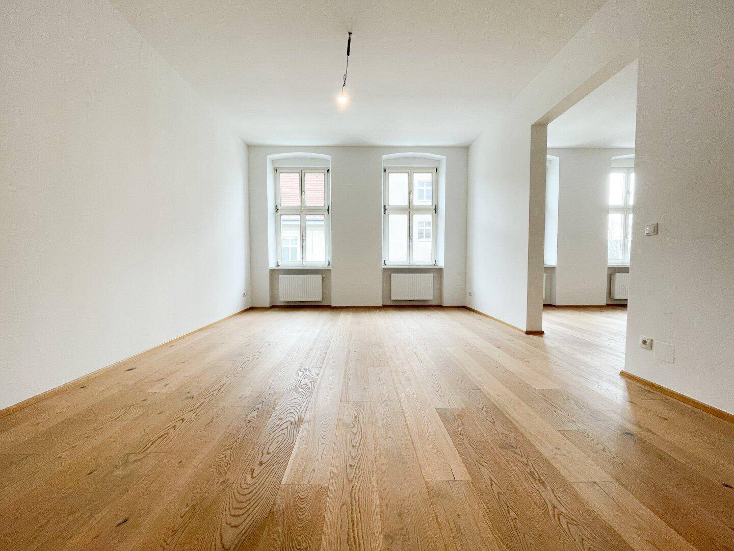 Geräumiges, helles Zimmer mit frisch verlegtem Parkettboden und Blick nach draußen.