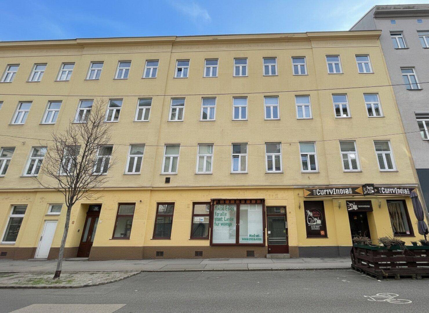 Die gesamte Fassade eines mehrstöckigen Wohn- und Geschäftshauses mit mehreren Fenstern und zwei Ladenlokalen im Erdgeschoss.