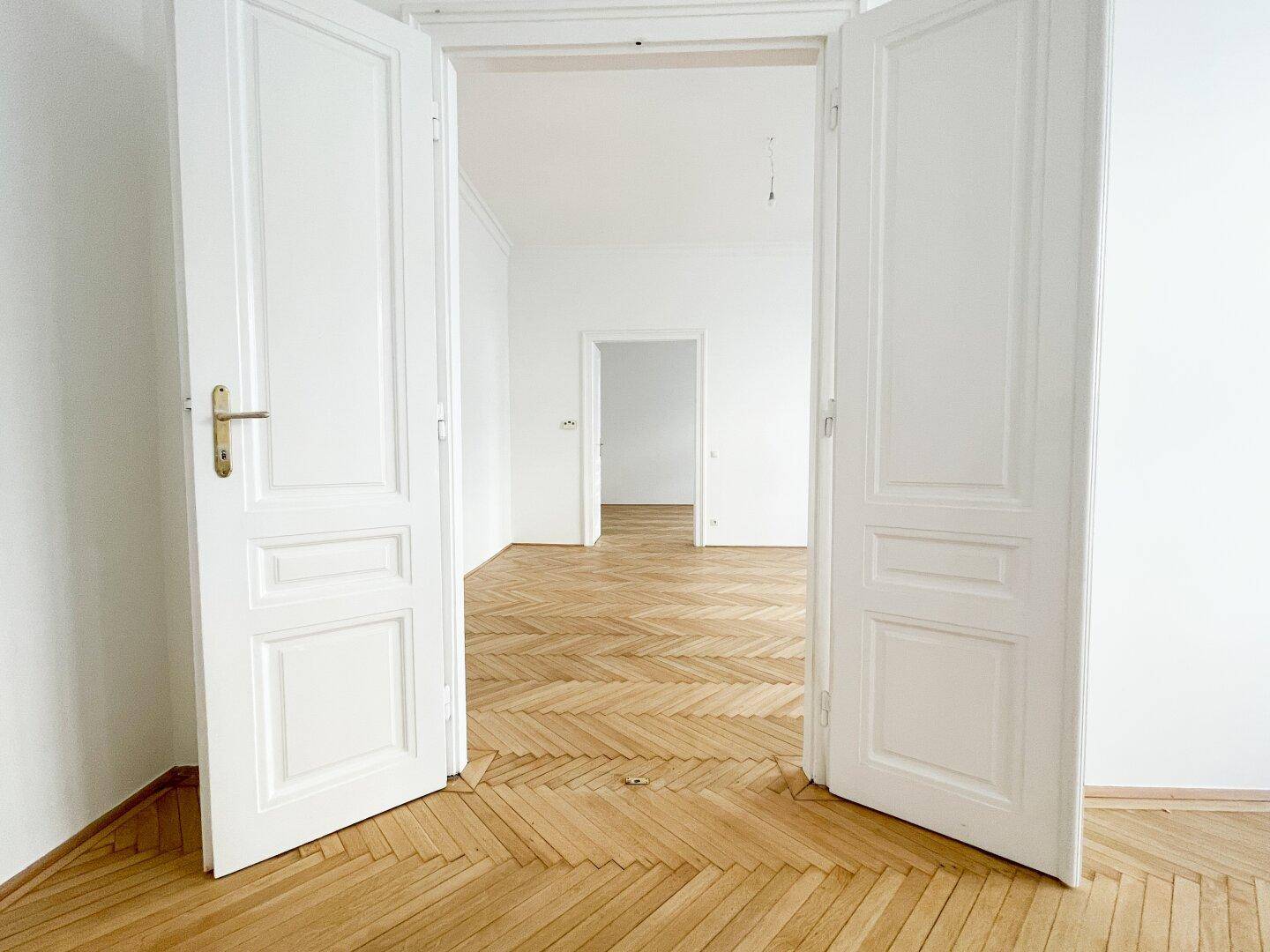 Blick durch offene Flügeltüren auf weitere Räume mit Fischgrätparkett und hohen Decken.