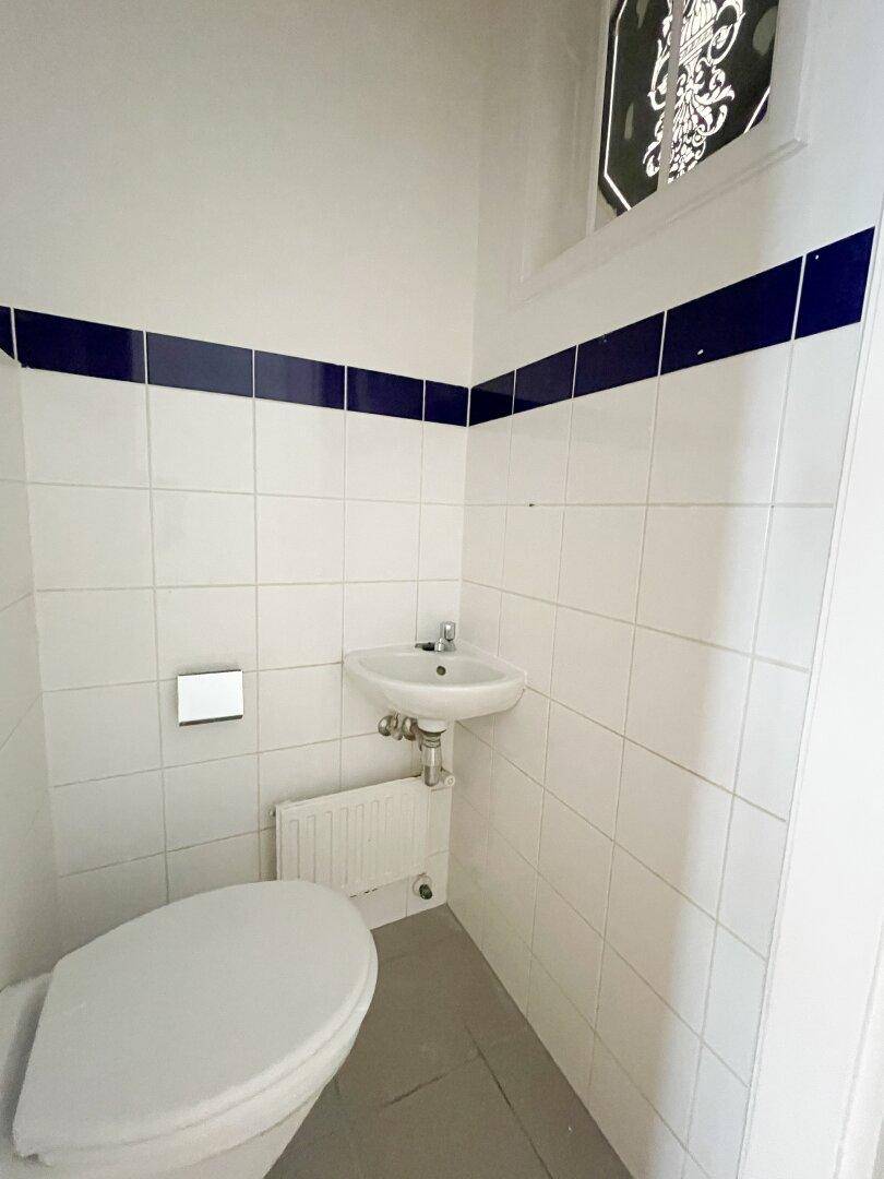 Kleines WC mit weiß gefliesten Wänden, blauen Akzentstreifen, Toilette und Handwaschbecken.