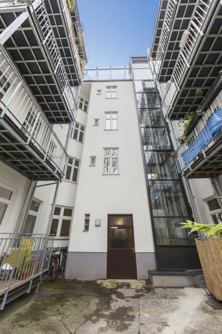 Innenhof eines Gebäudes mit externem Glasaufzug und mehreren Balkonen, die den Raum strukturieren.