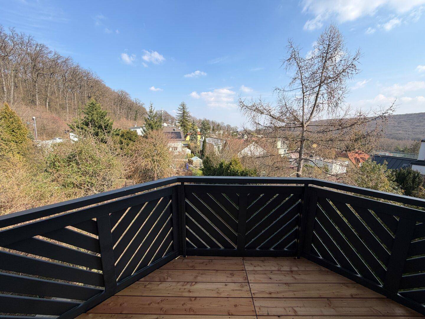 Geräumiger Balkon mit Holzboden und schwarzem Geländer, bietet einen weiten Blick ins Grüne.